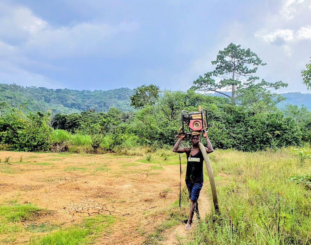 artisanal miner carrying water pump on head